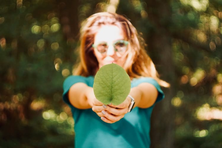 Frau in türkisem T-Shirt hält ein grünes Blatt vor die Kamera.  Mert Guller auf Unsplash