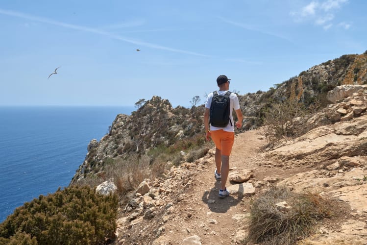 Entdecker durchquert atemberaubenden Klippenpfad mit Panoramablick auf den Ozean an einem Sommertag.
