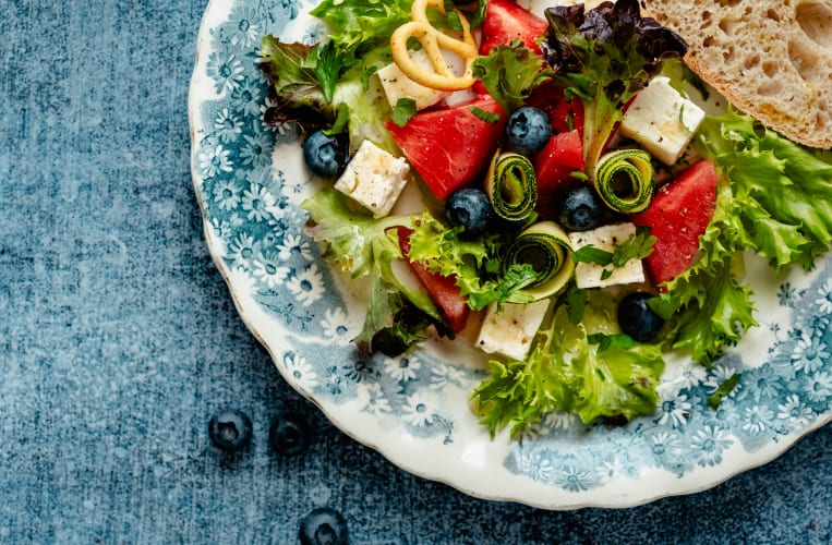 Blau-weißer Teller auf dem Salat angerichtet ist mit Zucchini, Heidelbeeren und Schafskäse null