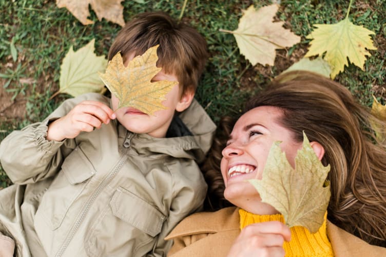 kleiner Junge und Mutter spielen mit Herbstlaub null