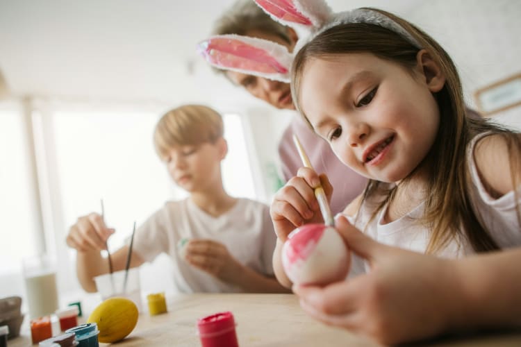 Mädchen mit Hasenohren auf dem Kopf malt ein Ei zu Ostern an null