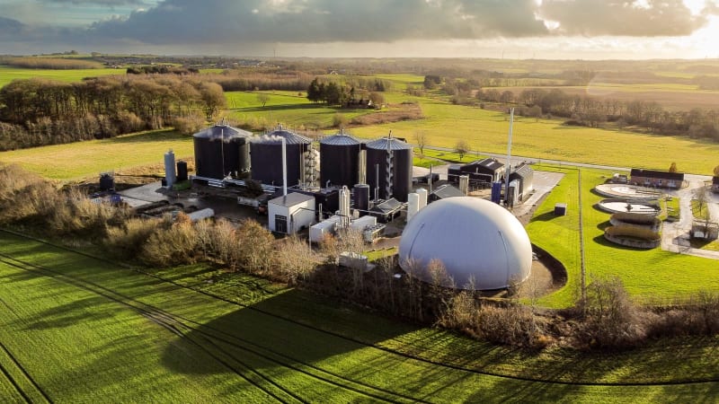 Drohnenaufnahme einer großen Biogasanlage inmitten grüner Felder in Dänemark, die die Infrastruktur für erneuerbare Energien und nachhaltige Technologien im ländlichen Raum verdeutlicht.