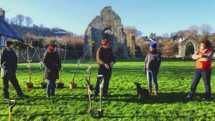 Five peoople about to plant trees, in front of a ruined building