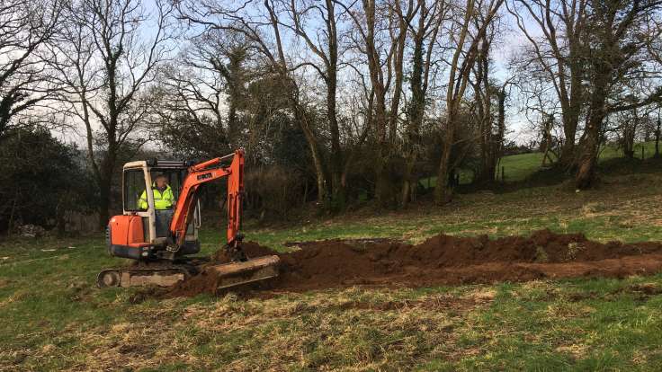 Man in mini-digger, scraping the top soil