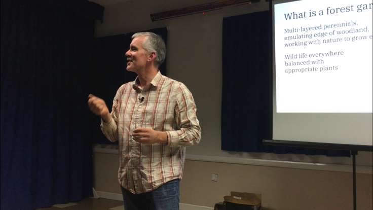 Man in checked shirt giving talk in front of screen