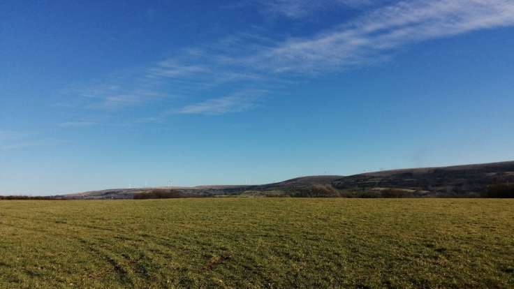 Bare green field with view beyond to bigger hills, blue sky