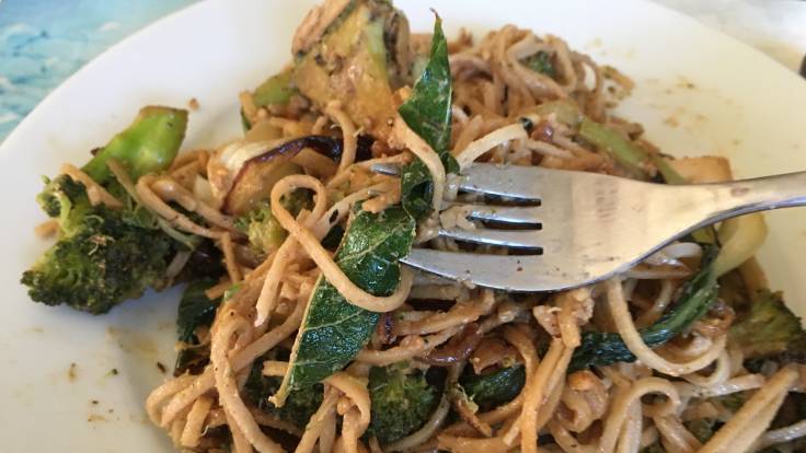 Close up of green leaf on fork with noodles on plate in background