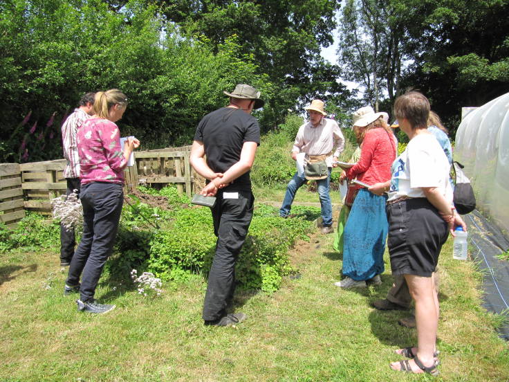 Group of people around raised bed by polytunnel and compost bins