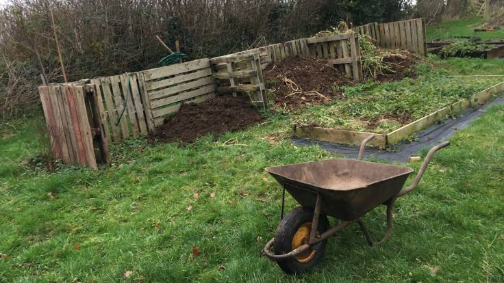 Old wheelbarrow in front of compost bays made from pallets