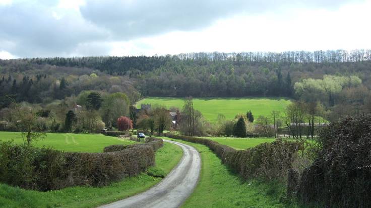 Country lane through wooded & pasture valley