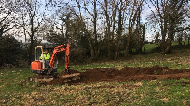 Digger scraping grass in field