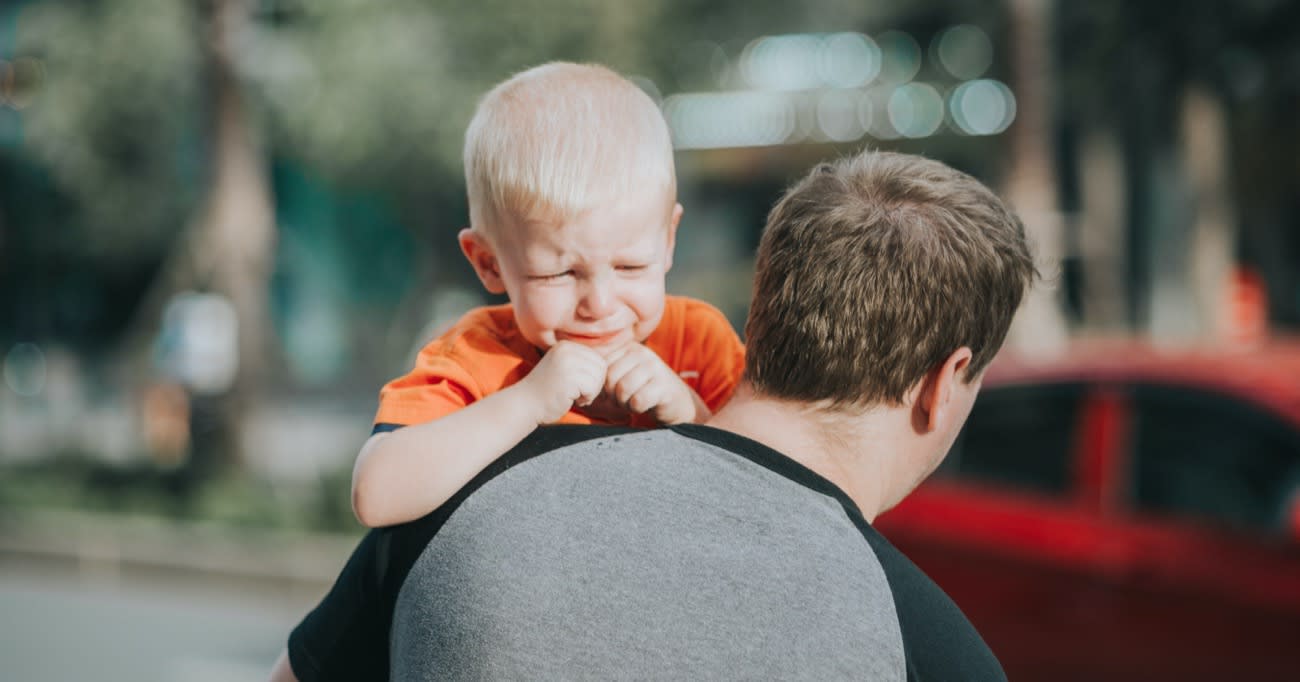 dad holding his young son over his should as the son cries