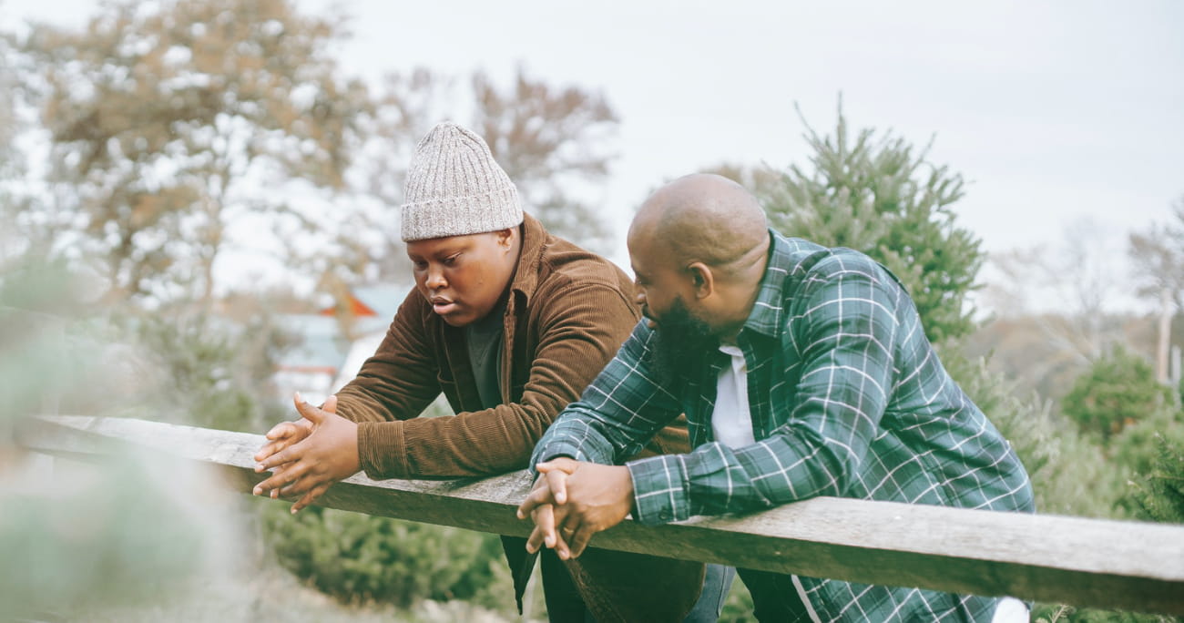 dad and son leaning on a fence and talking