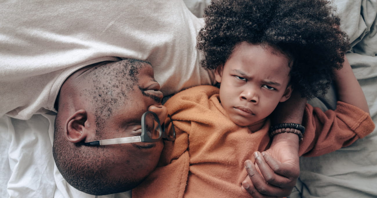 dad and son lying on bed with son angrily staring at camera