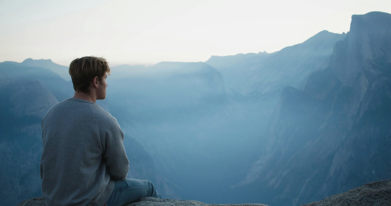 man sitting down looking over the edge of a cliff