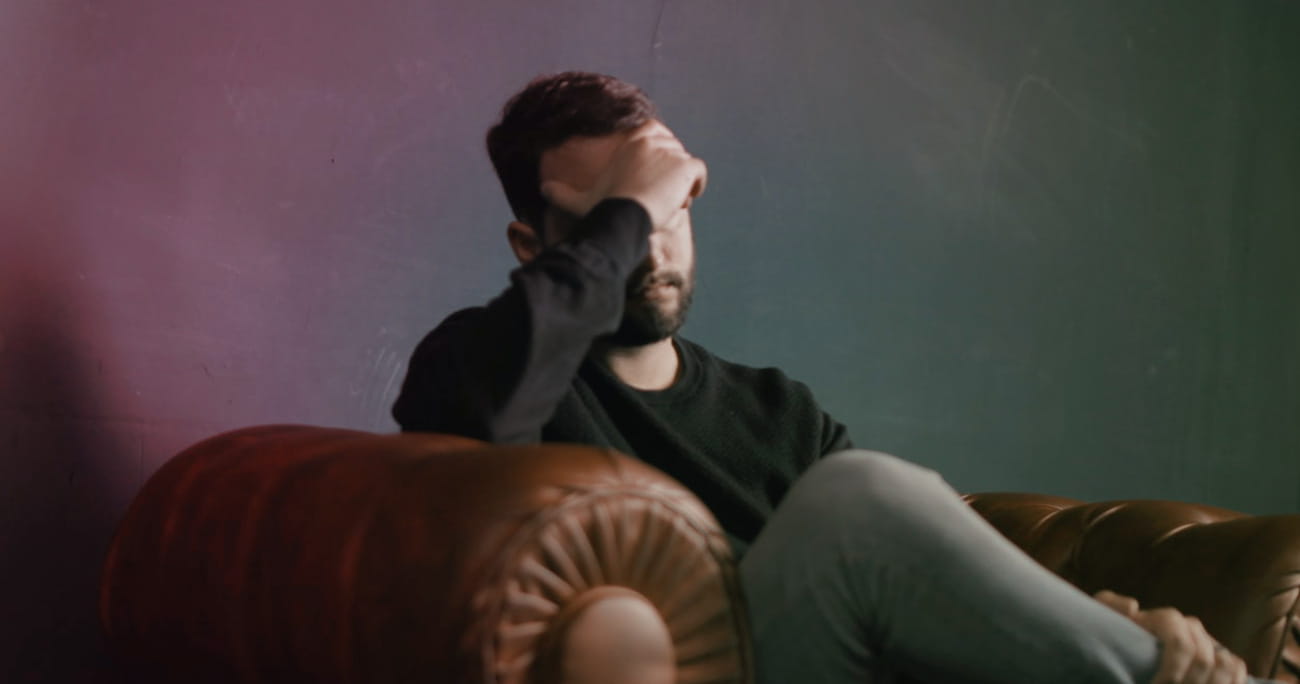 man in an arm chair holding his head in his hand
