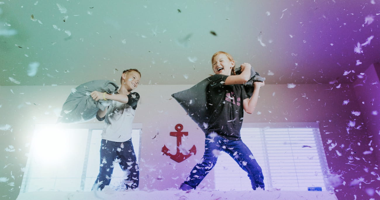 two children pillow fighting on a bed