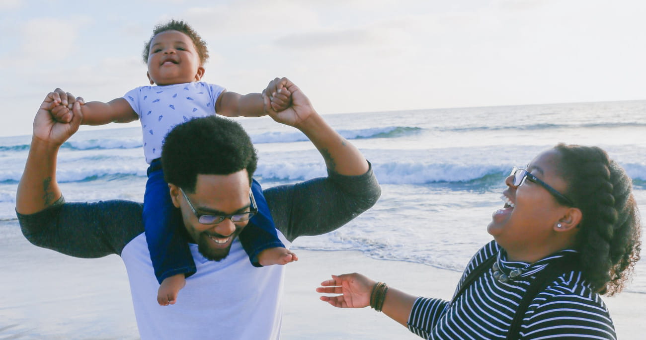 family on the beach with dad holding child on his shoulders
