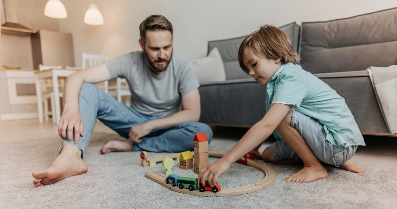 dad and young son playing with trains on the ground