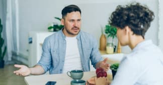 man sitting at his table looking angrily at his wife