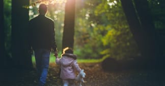 A dad walking through the woods holding his young daughter’s hand