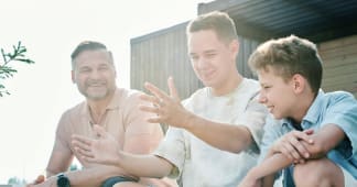 a dad sitting outside and laughing with his two teenage boys