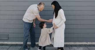 man and pregant wife with small child kissing mom's belly