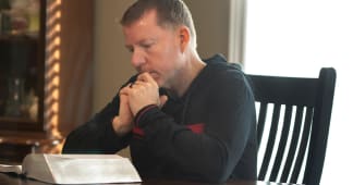 a man praying at his kitchen table with bible open