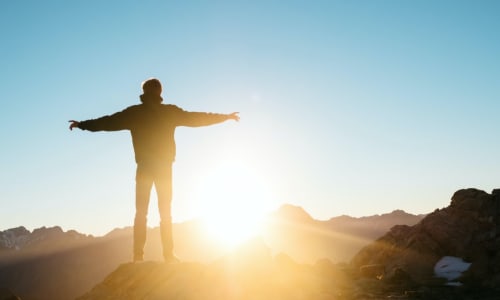 man standing on a hill looking at the sunset