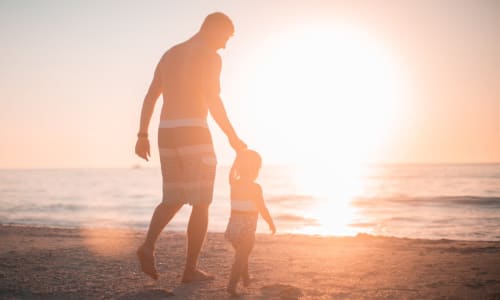 dad and son walking on the beach together at sunset