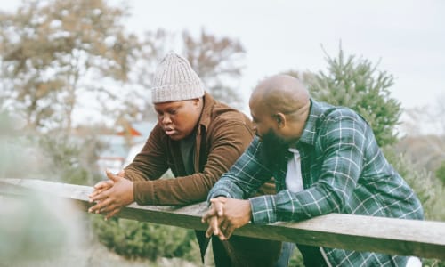 dad and son leaning on a fence and talking