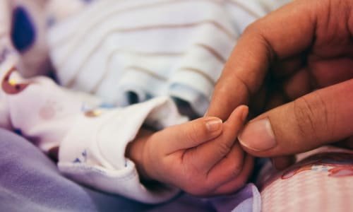 infant child’s hand holding an adult’s hand