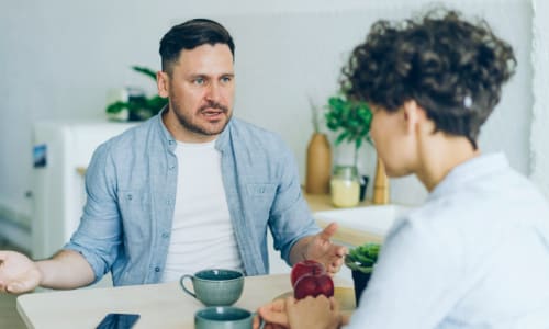 man sitting at his table looking angrily at his wife