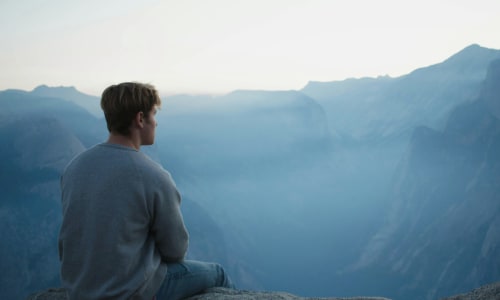 man sitting down looking over the edge of a cliff