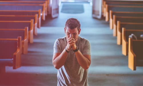 man kneeling in prayer in the front of a church