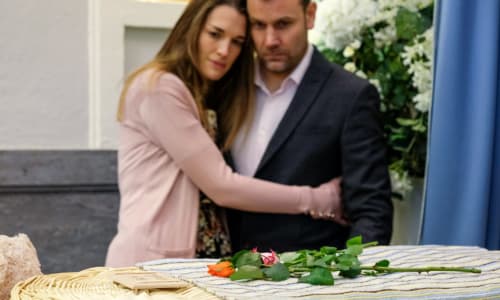 a mom and dad crying while looking on an infant casket