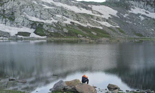 man sitting on a rock in front of a mountain lake