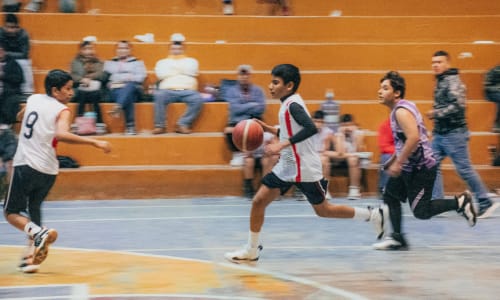 boys playing basketball with parents cheering them on