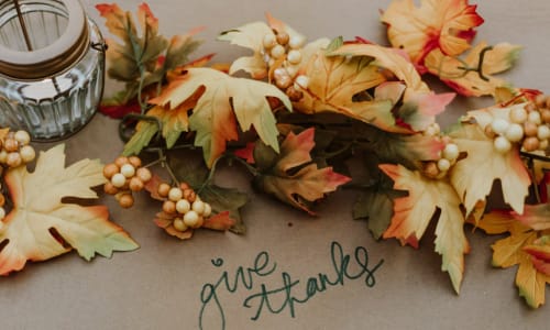 the words 'give thanks' written out on a table with fall leaves surrounding it