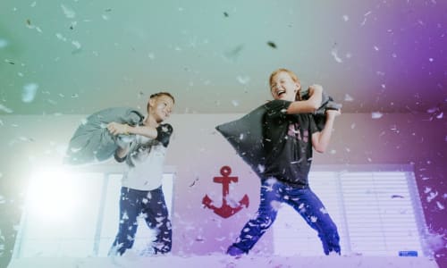 two children pillow fighting on a bed