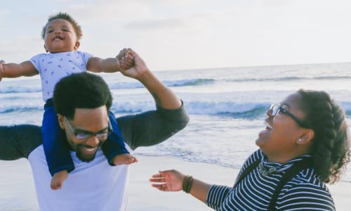 family on the beach with dad holding child on his shoulders
