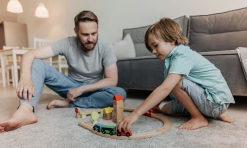 dad and young son playing with trains on the ground