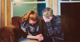 Mom and daughter on a couch crying with heads bowed