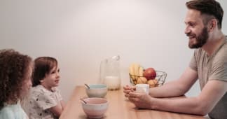 Dad sitting across the table from his two young children talking