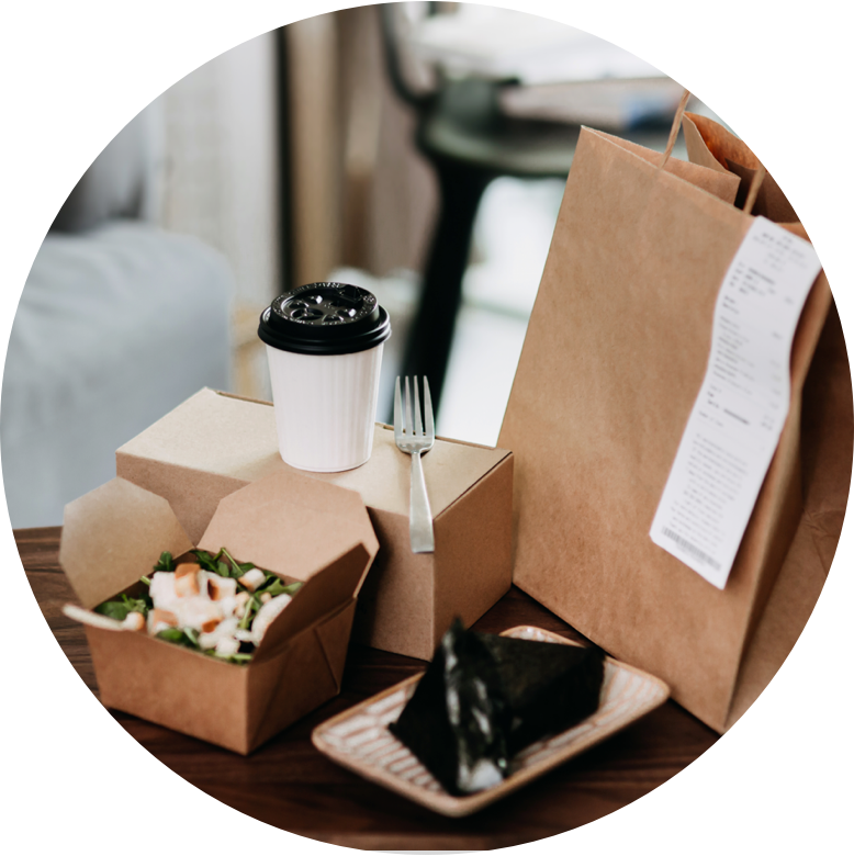 A brown food bag with a receipt attached alongside an open salad box as well as a closed box with a fork and coffee on top.