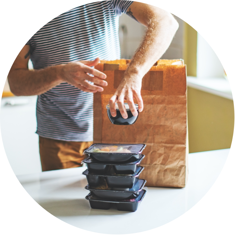 Man standing removing and stacking food items out of a brown paper bag.