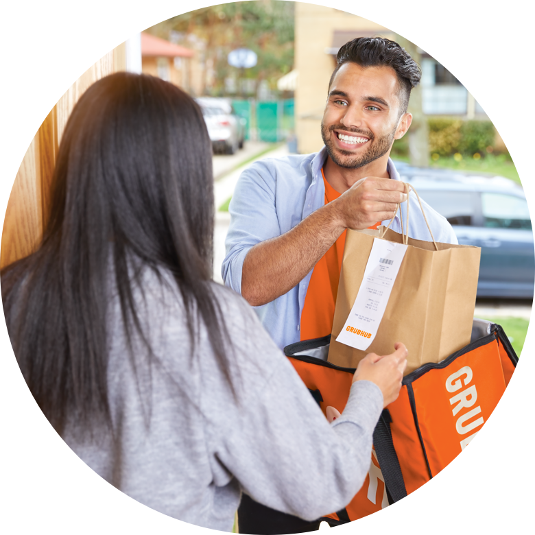 Grubhub delivery driver smiling handing a bag of food to a woman at her front door.