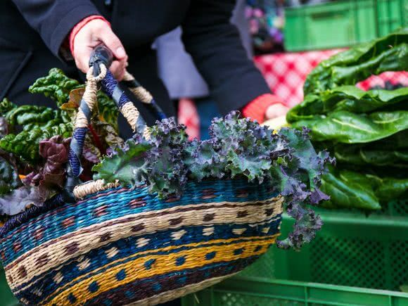 Frau kauft am Markt ein und hält einen Korb in der Hand, gefüllt mit frischem Mangold