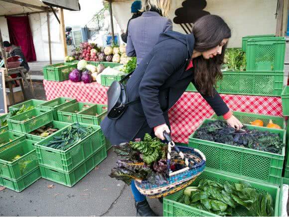 Frau wählt an einem Wochenmarkt-Stand frische Blattgrünsorten aus.