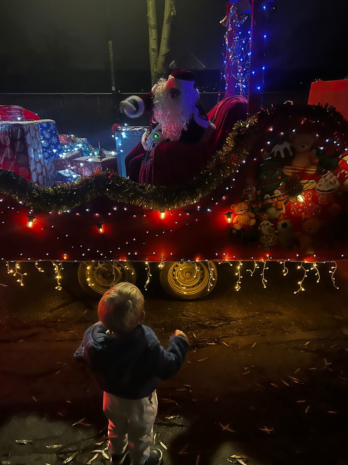 A young child watching Santa pass in his illuminated sleigh